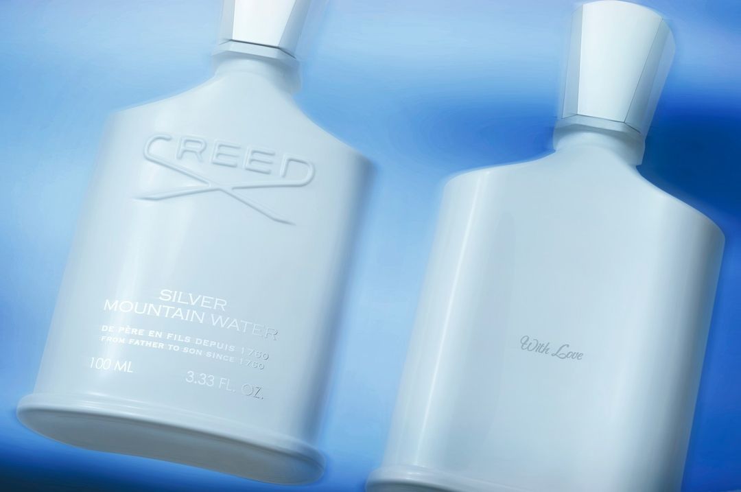 Two Creed Silver Mountain Water perfume bottles stand against a soft blue background, showcasing a clean, minimalist aesthetic.