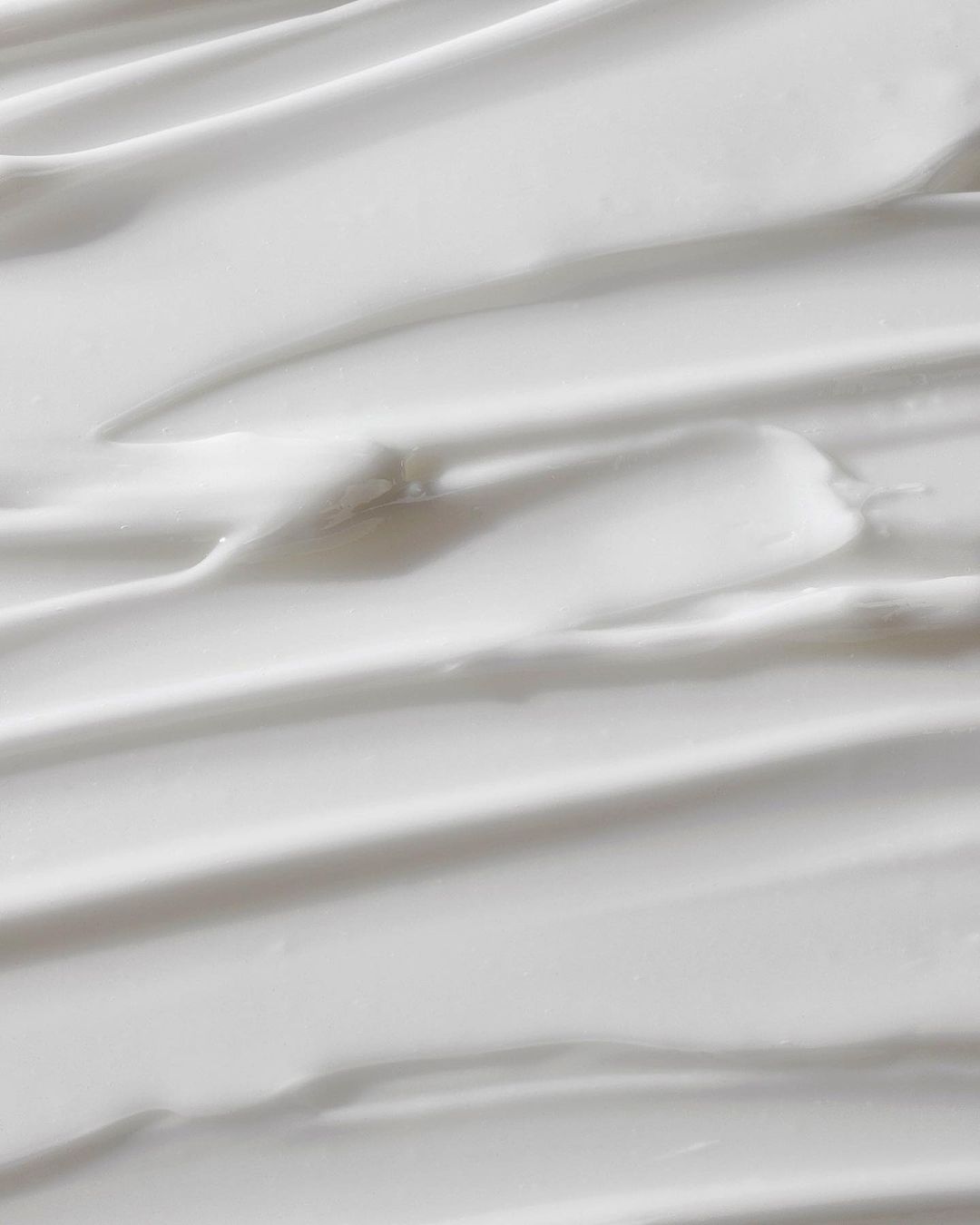 Close-up of white cream texture with smooth, curved lines, providing a clean and minimalist background for beauty or skincare concepts.