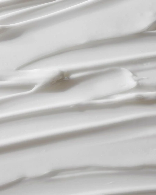 Close-up of white cream texture with smooth, curved lines, providing a clean and minimalist background for beauty or skincare concepts.