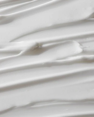 Close-up of white cream texture with smooth, curved lines, providing a clean and minimalist background for beauty or skincare concepts.