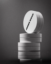 A stack of four round white cosmetic jars with Jones Road branding, photographed in a dramatic low-key monochrome studio setting.