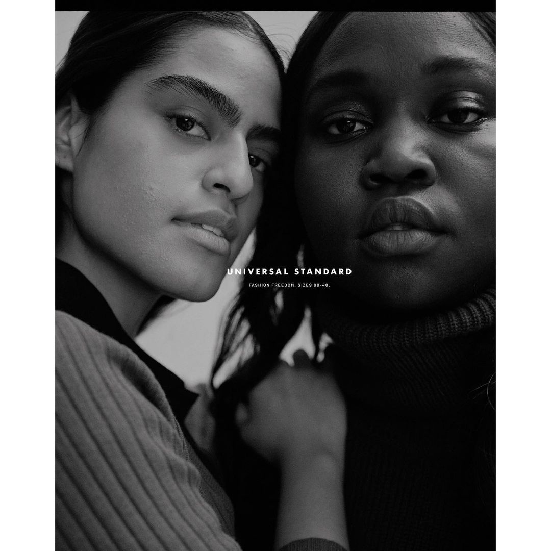 Monochrome portrait of two adult women, one with lighter skin and one with darker skin, posing closely together, shot in studio.