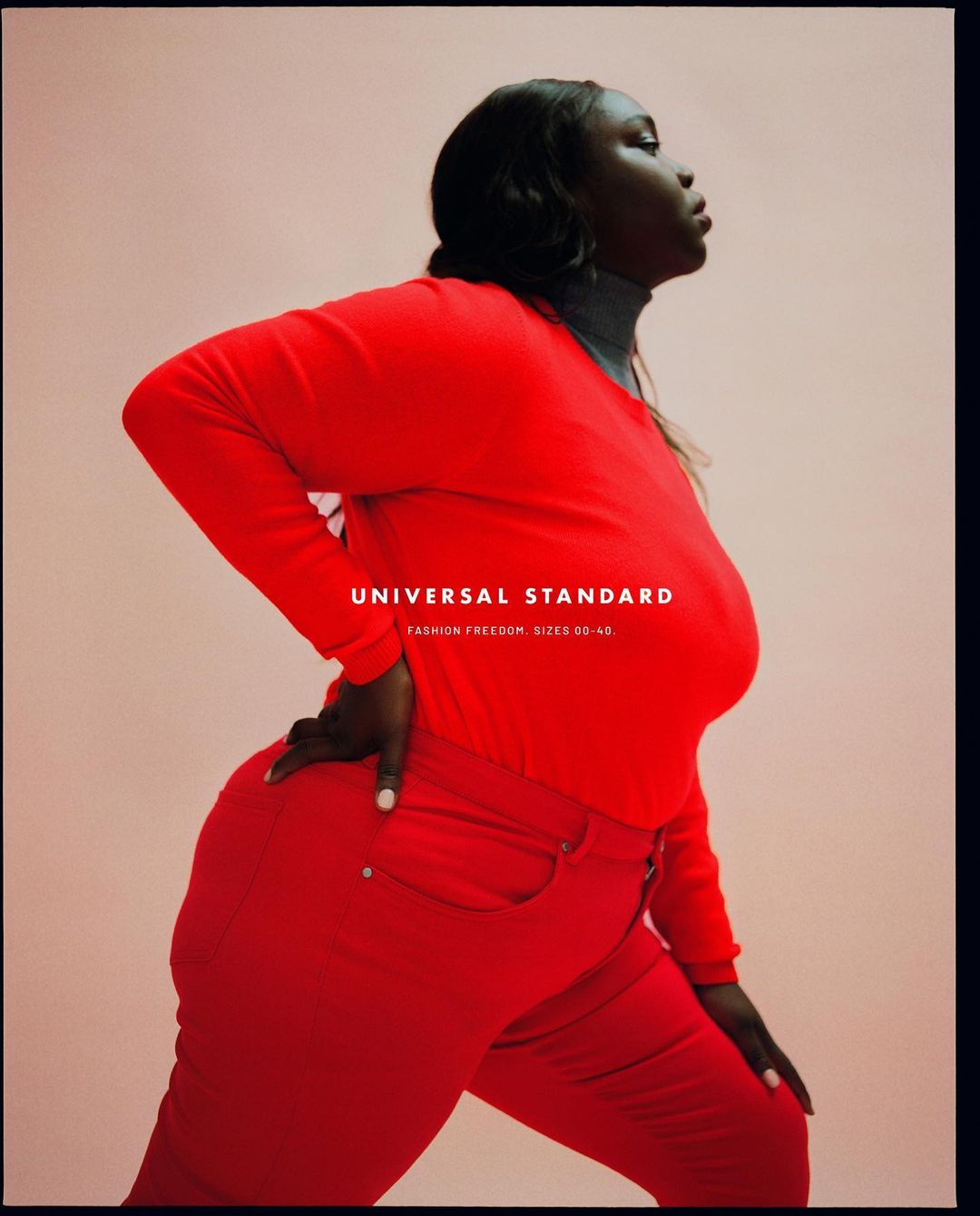 Portrait of an African-American woman wearing a red long-sleeved shirt and red pants in a studio setting, posing against a light peach background.