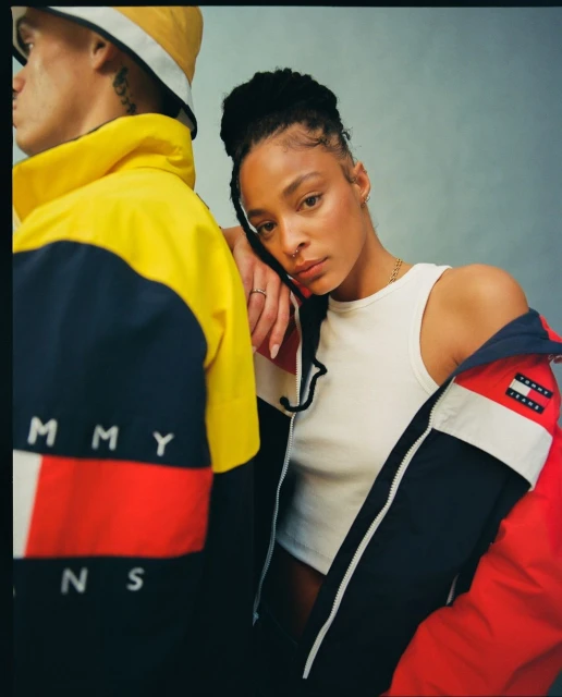 Fashion shot featuring a mixed-race woman in a white top and an open jacket, and a man wearing a yellow bucket hat and jacket.