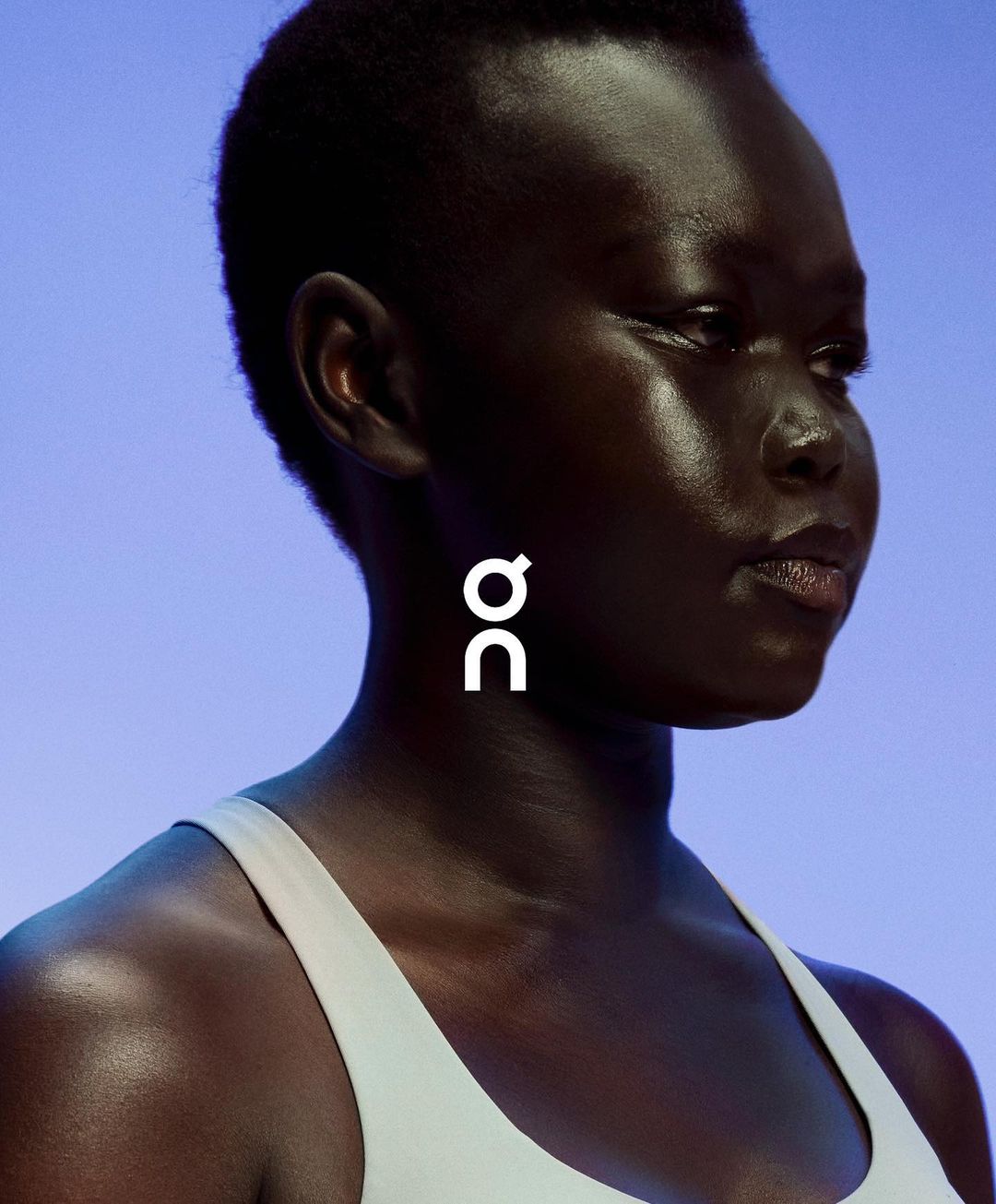 Close-up of a dark-skinned woman in athletic wear against a light blue background with the white On Running brand logo.