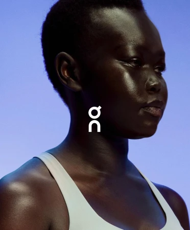 Close-up of a dark-skinned woman in athletic wear against a light blue background with the white On Running brand logo.