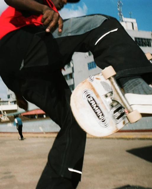 A person rides a skateboard on a concrete surface near a building, captured from a low angle with a clear blue sky backdrop.