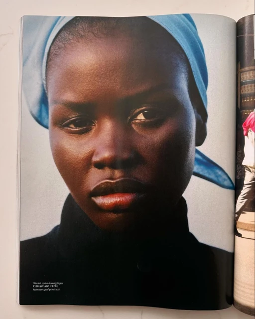 Close-up portrait of a woman with dark skin and a blue headscarf looking directly at the camera; a fashion or beauty editorial shot.