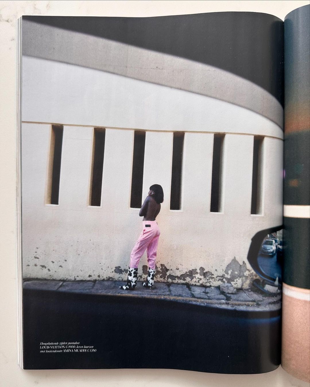 Adult female model posing in front of architectural structure with light and shadow and wearing pink pants and cow print boots.