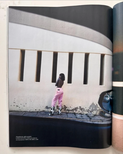 Adult female model posing in front of architectural structure with light and shadow and wearing pink pants and cow print boots.
