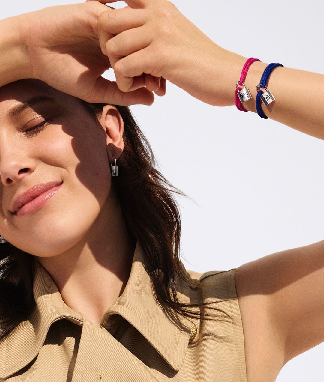 Close-up of a light-skinned adult female wearing a tan jacket and silver earrings, showcasing pink and blue bracelets with silver charms.