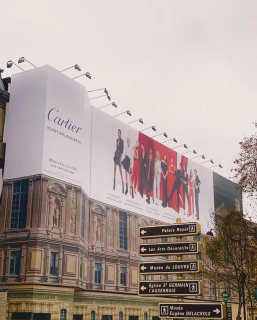 Outdoor billboard in Paris promotes Cartier with a group of fashion models dressed in black, red, and white formalwear.