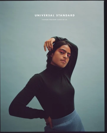 Fashion shot of a woman with pink eyeshadow wearing a black turtleneck and blue skirt, posing against a light blue backdrop.