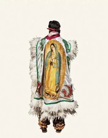 Person in ceremonial Aztec dress with an image of the Virgin of Guadalupe on a white background, rear view. 