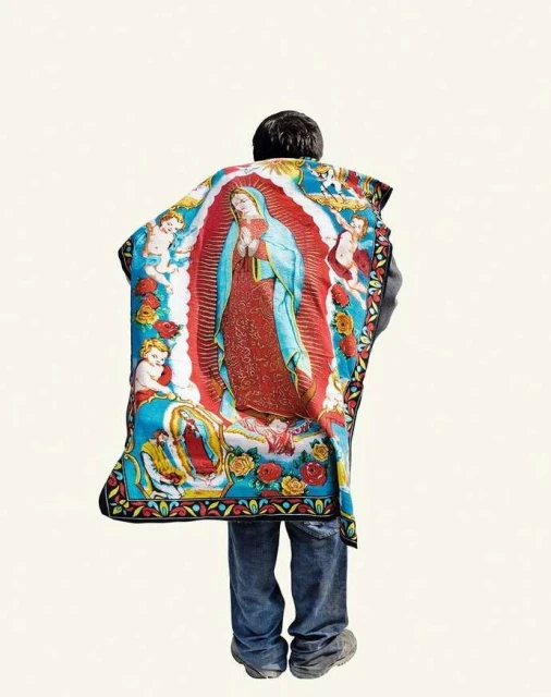 Person wearing a colorful poncho featuring the Virgin Mary and angels stands against a white background, showcasing a unique blend of fashion.