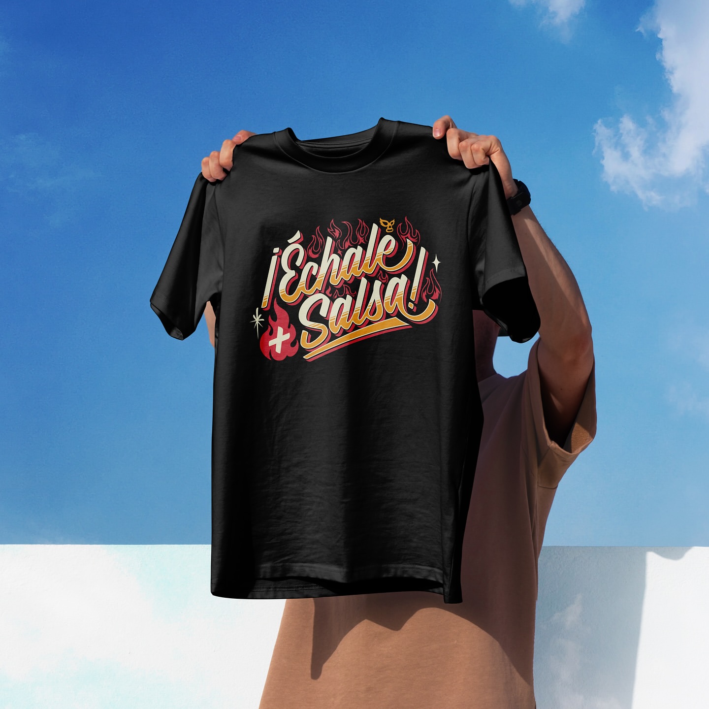 Black t-shirt featuring 'Echale Salsa' graphic text held up against a partly cloudy blue sky, showcasing apparel and outdoor setting.