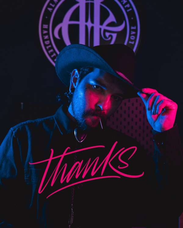 Bearded man in cowboy hat wearing a black shirt with 'Thanks' printed on it, neon-lit face, and a decorative background emblem.