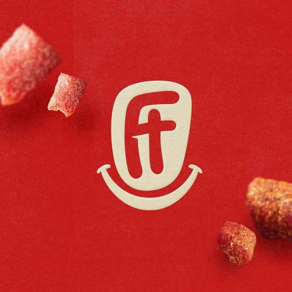 Close-up of a red background featuring a cream-colored logo with a smiling face, accompanied by two pieces of red candy.