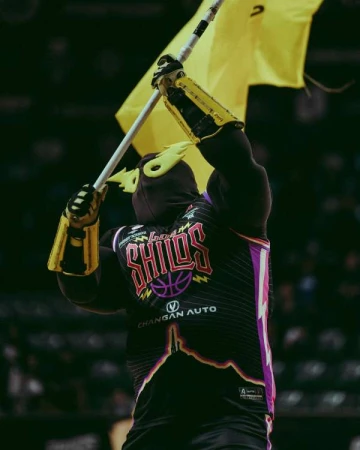 Mascot in jersey holding up a yellow flag during a basketball game, with Changan Auto logo and SHIOS text visible on the jersey.