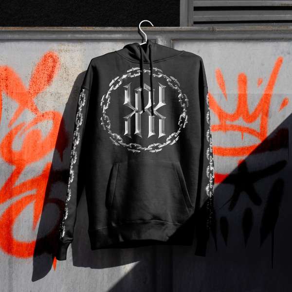Black hoodie with a silver chain design on a hanger against a graffiti wall, showcasing fashion and urban style in an outdoor setting.