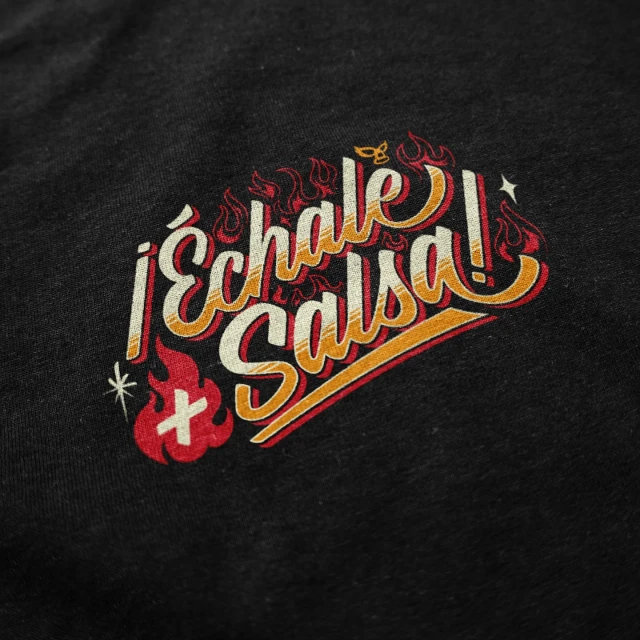 Close-up of a dark heather T-shirt featuring a graphic print with the text "Échale Salsa!" stylized with flames and decorative elements.