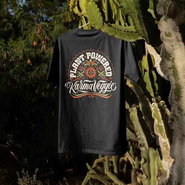 Black t-shirt with a plant-powered Karma Veggie graphic design hanging against an outdoor green foliage background.