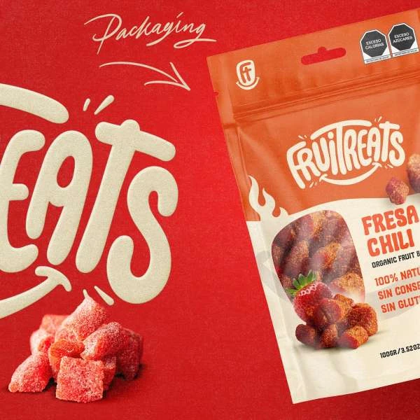 Promotional shot of Fruitreats fresa chili snacks in packaging against a red background with product info and branding details.