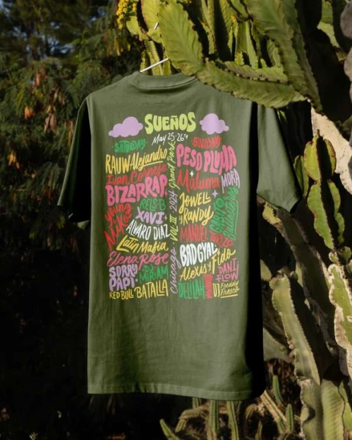 Olive green t-shirt featuring 'Sueños' festival lineup of musicians hanging against a blurred background of trees and cactus.