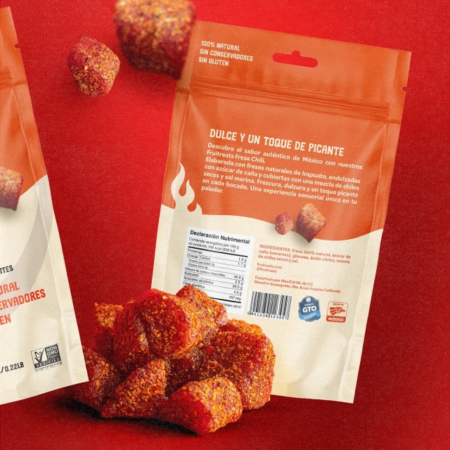 Eye-level studio shot of spicy strawberry candies, in and out of orange branded packaging, set against a vibrant red background.
