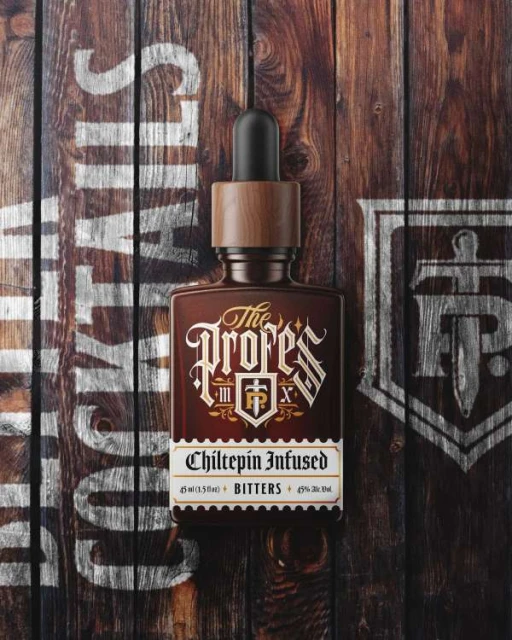 Overhead studio shot of a dark brown bitters bottle with a wood grain label, against a wooden background with white painted text.