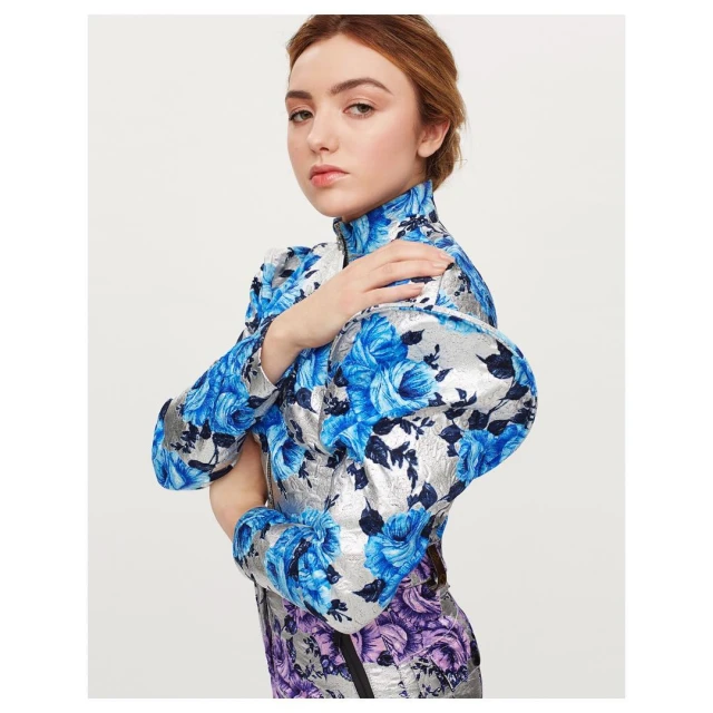 Attractive young woman poses indoors in a floral-patterned dress with puffy sleeves against a plain white backdrop. Fashion photography.