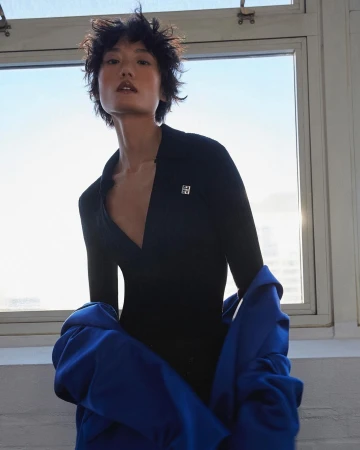 Model with short dark spiky hair wearing a black polo shirt and blue jacket against a bright window by Aingeru Zorita
