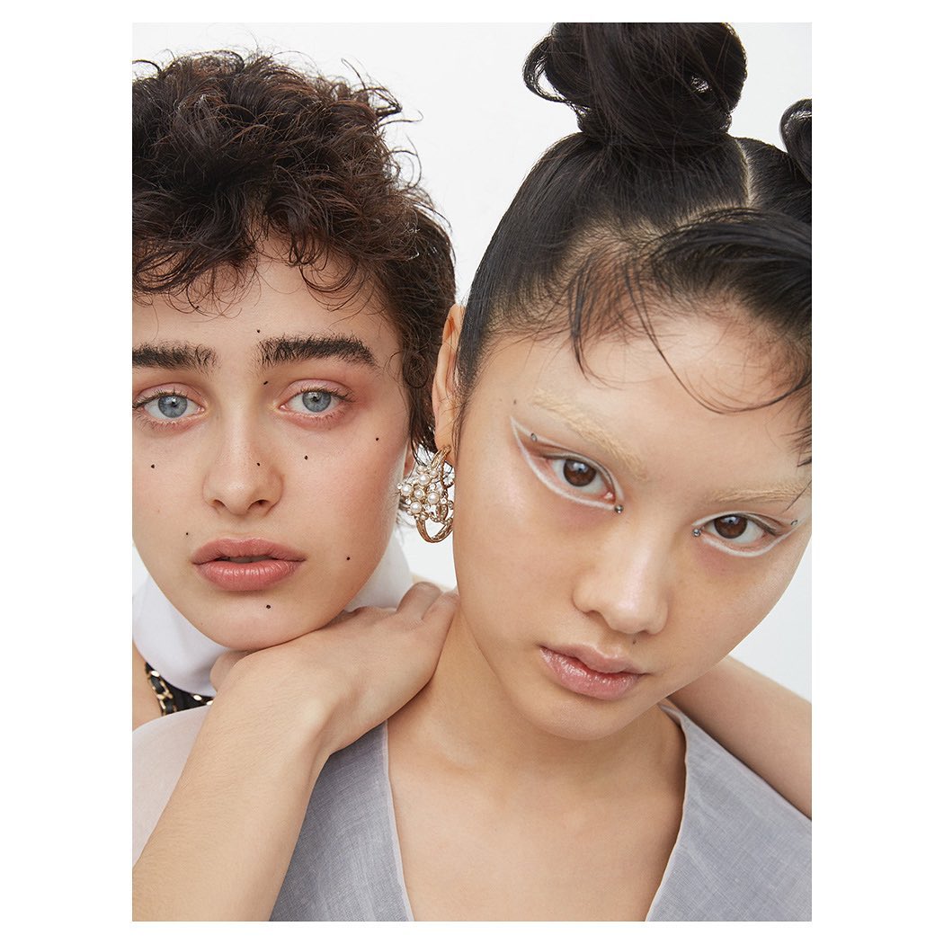 Two women with makeup and avant-garde earrings in a fashion forward portrait against a white background, close-up. Beauty and fashion.