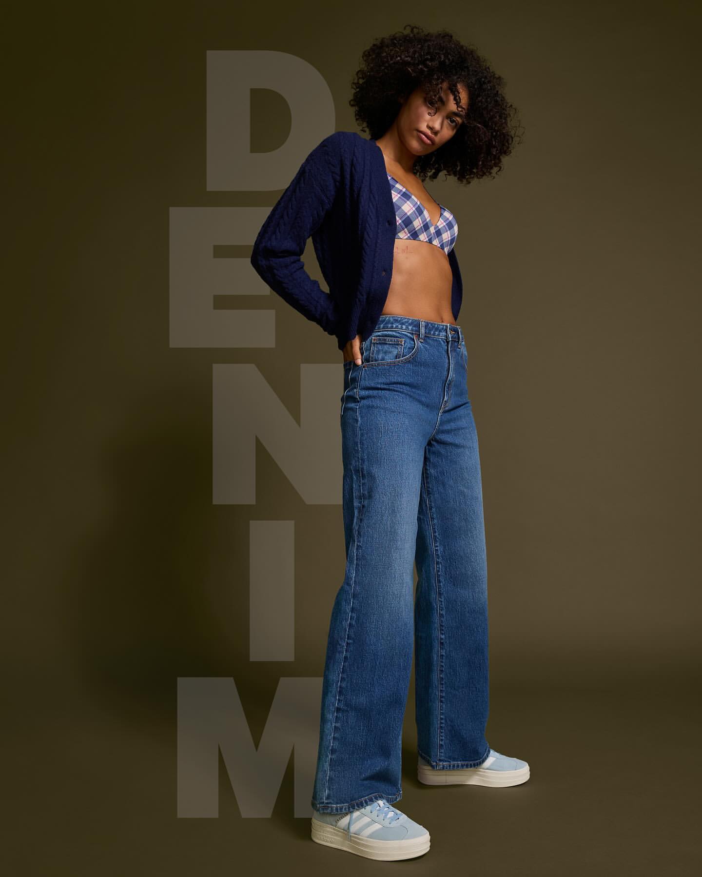 A stylish woman models flared denim jeans, a blue cardigan, and platform sneakers against an olive-green background with 'DENIM' text overlay.