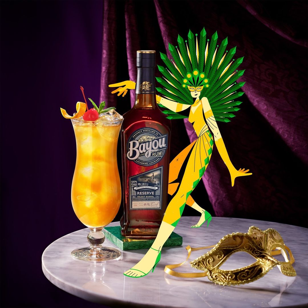 Rum cocktail on marble table next to Bayou Rum bottle and Mardi Gras mask. Festive purple curtain background. 