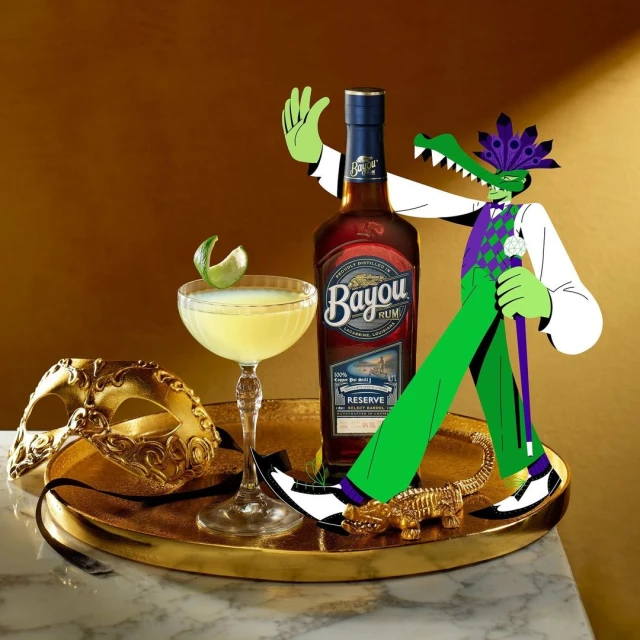 Still life of Bayou Rum bottle, cocktail, and Mardi Gras mask, with illustration of alligator in suit, on a gold tray.