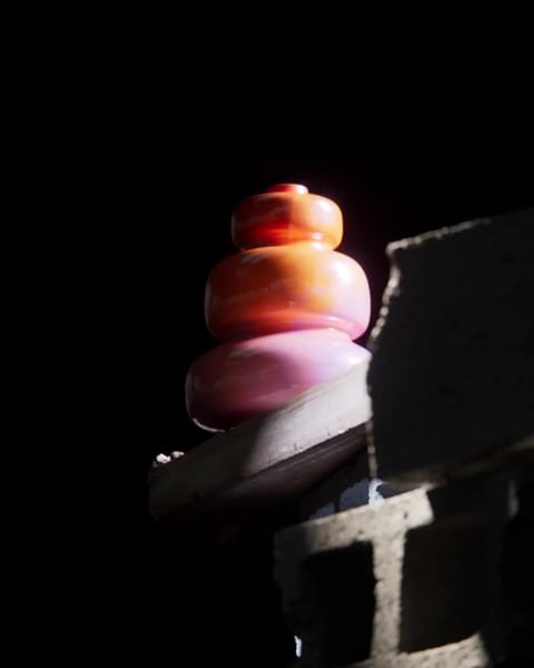 Abstract still life of stacked colorful glass-like forms in the dark against a rough, gray concrete block wall with shadows.