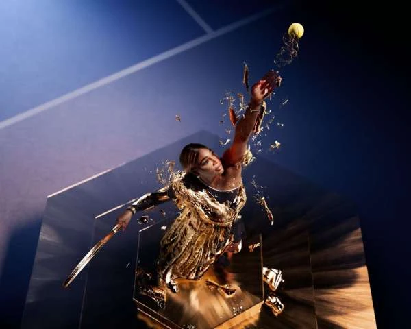 Action shot of a woman in a gold dress hitting a tennis ball with a racket, captured against a backdrop of geometric shapes.