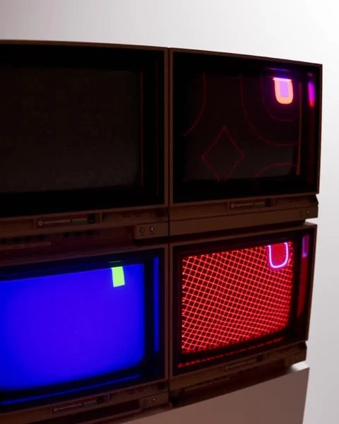 A stack of four vintage televisions with abstract colorful displays, set against a plain white background in a studio.