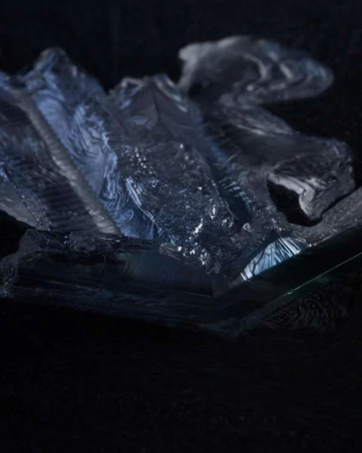 Abstract translucent sculptural form with patterned surface on clear surface in studio with dark background. Glass sculpture art.