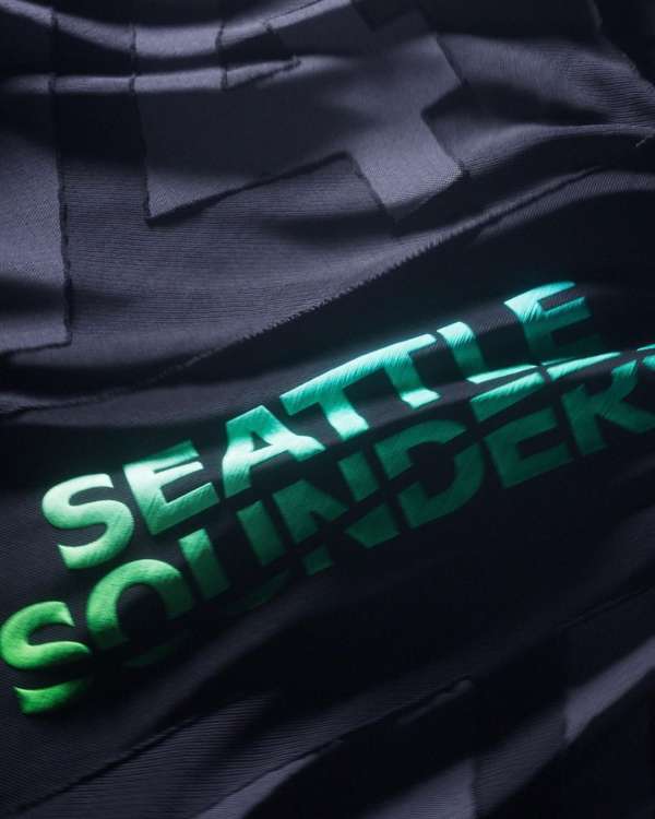 Close-up on a Seattle Sounders FC garment featuring a black textured material with tonal black patterns and green team lettering.