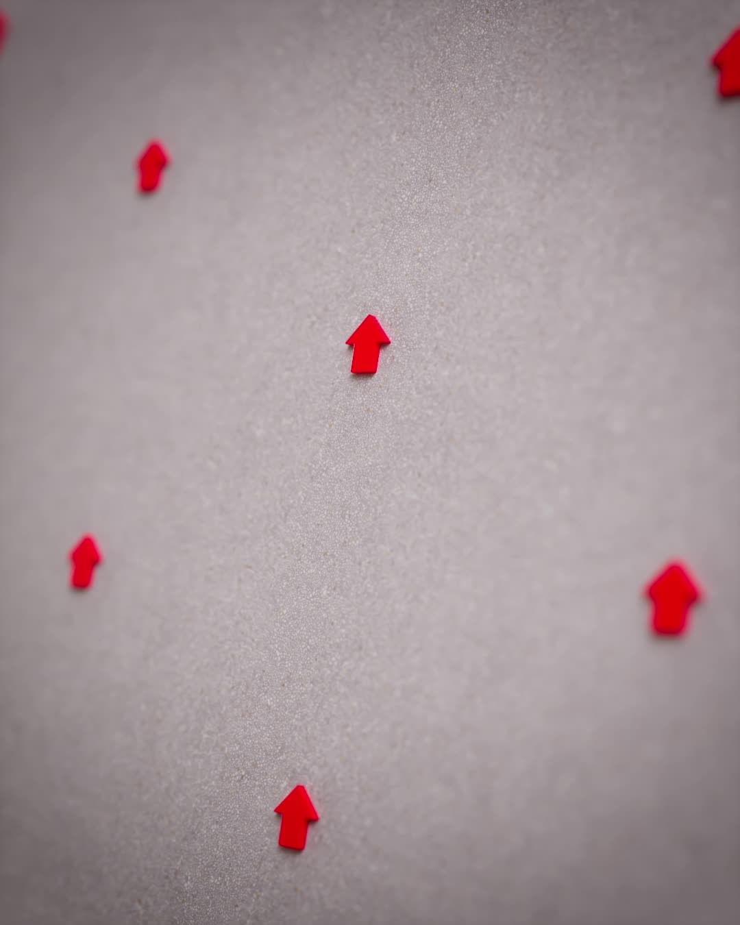 Red arrows pointing upward arranged in a pattern on a gray surface, creating a directional and visually repetitive composition.