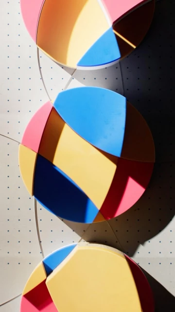 Abstract geometric art featuring intersecting circles in pastel hues of pink, yellow, and blue, arranged vertically on a white dotted background.