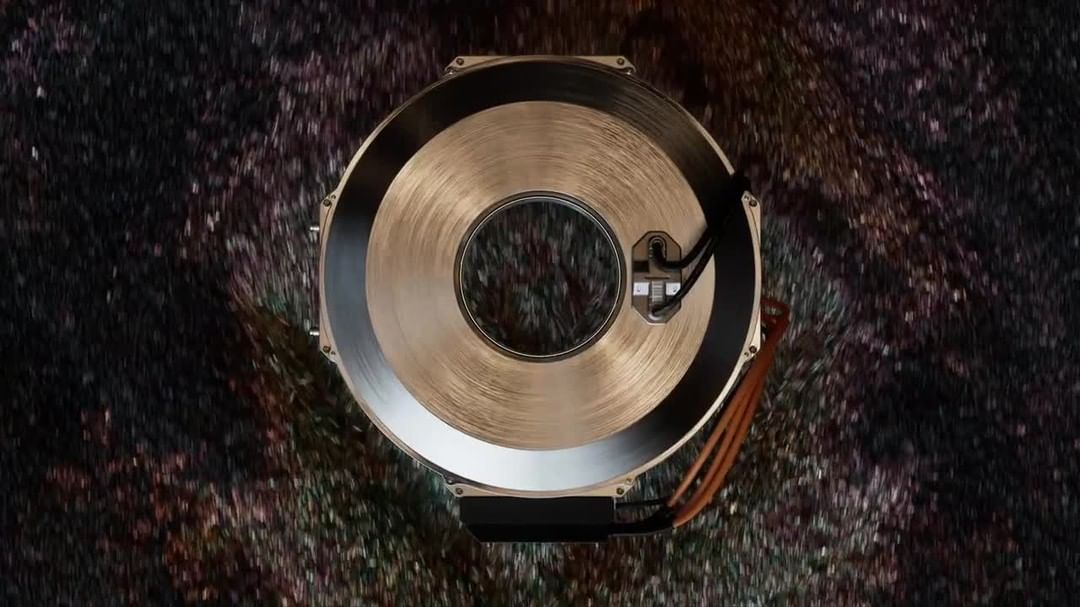 Close-up overhead shot of a metallic disc with a central hole, cables, and a black backing against a blurred, multi-colored backdrop.