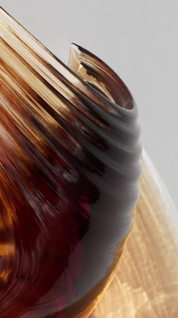 Close-up of a decorative glass vase featuring a swirl pattern with amber and brown tones against a neutral background. The vase is translucent.