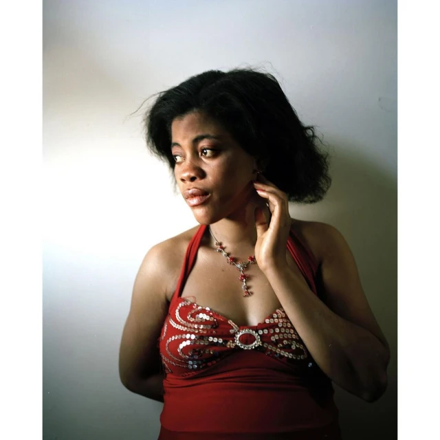 Glamorous African-American woman in a red halter dress with sparkling embellishments, looking left in a photo studio setting.