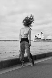 Model with long curly hair blowing in the wind wearing textured patterned trousers near Sydney Harbour