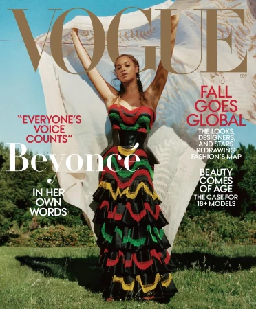 Beyoncé on the September cover of Vogue magazine wearing a strapless black, red, yellow, and green dress with a white shawl outdoors.