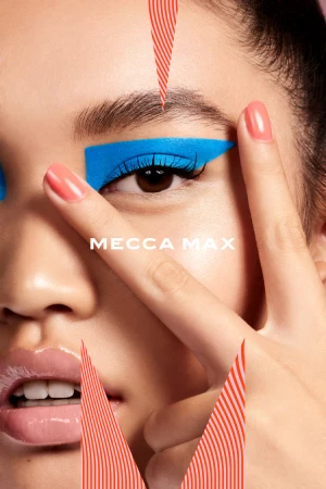 Close-up of a model's face with bright blue geometric eye makeup and peach-colored glossy nails, featuring the text MECCA MAX.