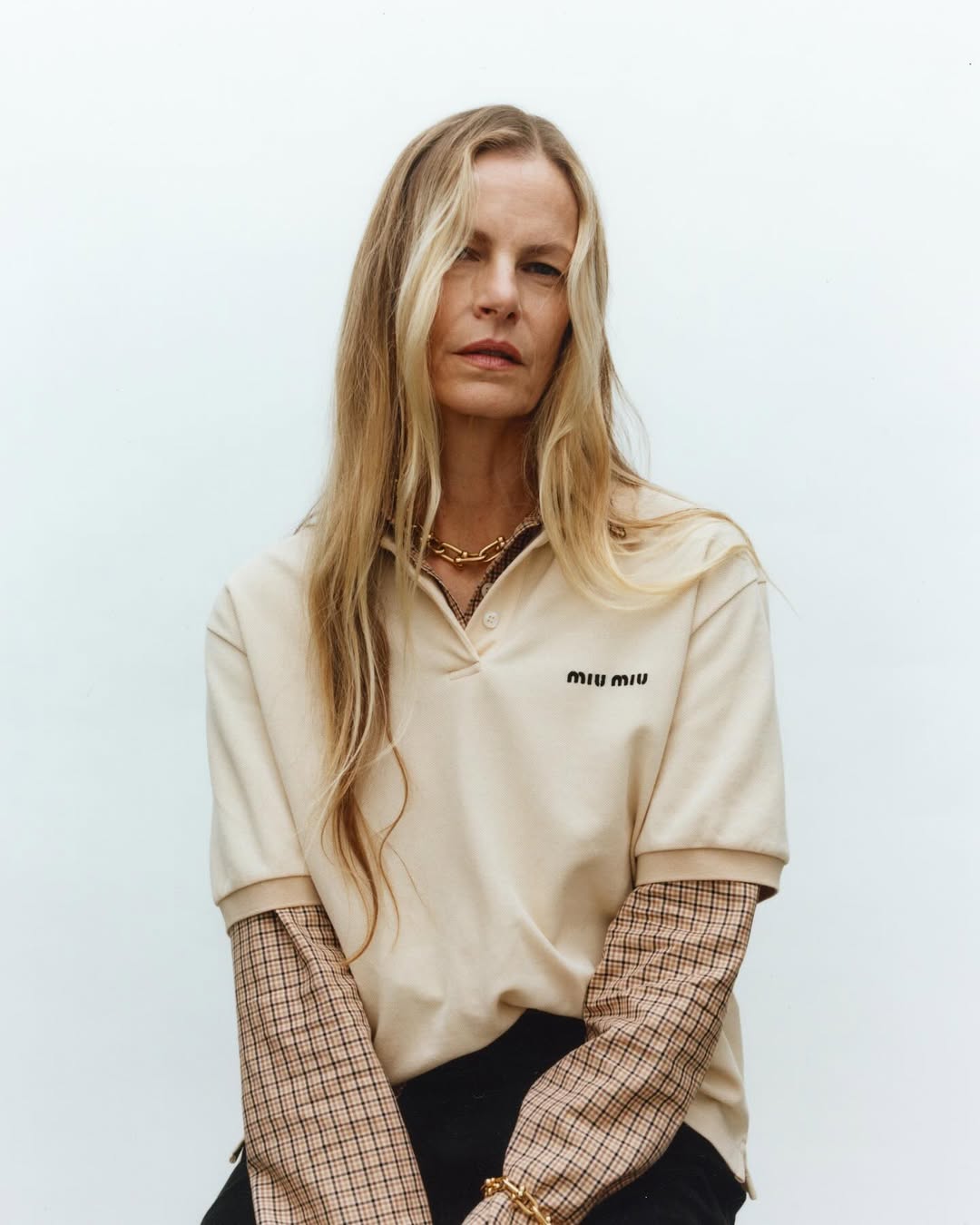 Portrait of an adult female with long blonde hair wearing a beige polo shirt with black pants against a plain white background.